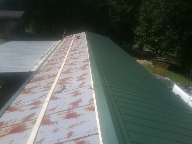 Old rusted panels beside newly installed green metal roofing — Wind Damage Roof Repair by Roofing Brothers in Hudson