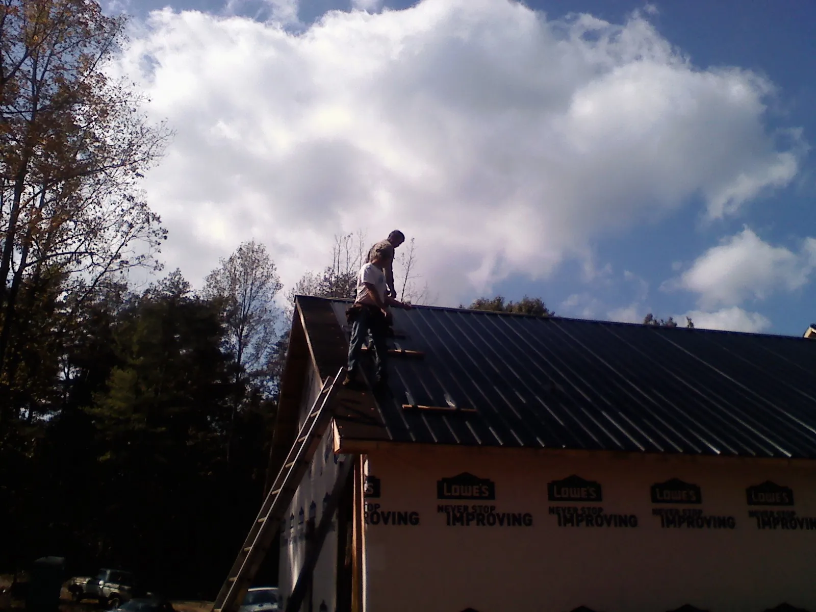 Roofer fastening dark metal panels high against a cloudy sky, from a Roof Inspection job in Hudson